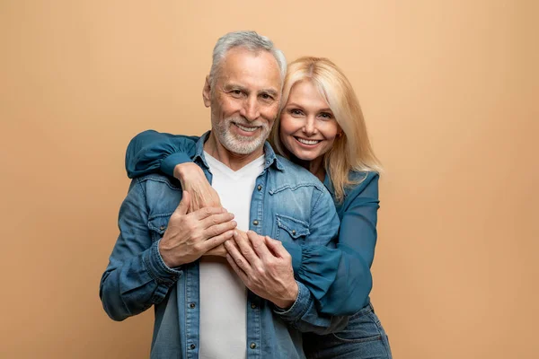 stock image Portrait of loving cheerful beautiful senior couple grey-haired handsome man and blonde pretty lady bonding on colorful pastel studio background, smiling at camera. Love, affection, marriage