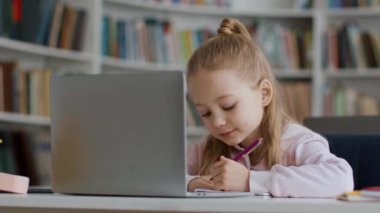 Geleneksel ve modern çalışma tekniklerini birleştirmek. Dizüstü bilgisayar üzerine yoğunlaşmış küçük kız okuma görevi ve metin kitabı, modern sınıfta çalışma, çekim takip, yavaş çekim, serbest alan