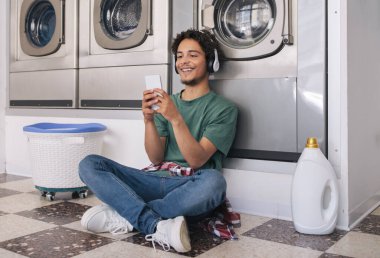 Kolay Çamaşır. Çamaşırları çamaşır makinesinde yıkanırken, hafta sonu tatili ve ev işlerinin keyfini çıkarırken akıllı telefon kullanan mutlu adam bekliyor.