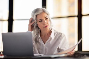 Girişimcilik Evrakları Sorunu. Mutsuz iş kadını bilgisayarın önünde çalışan kağıt faturalarına ve belgelere bakıyor modern ofisteki vergilerle sorunu var.