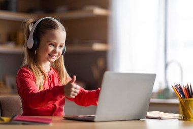 Sanal Sınıf. Bilgisayar ekranına bakan, başparmağını kaldıran, kulaklık takan, internetteki başarılarını kutlayan, internetteki boşluğu kopyalayan küçük kız öğrenci.