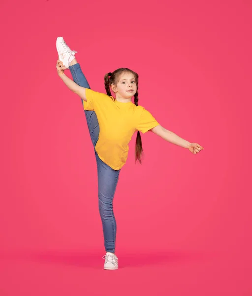 スポーティ女の子作る体操 柔軟なPreteen女性の子供持ち上げる彼女の足でツインと見るカメラ ストレッチとポーズオンピンクのスタジオの背景 — ストック写真