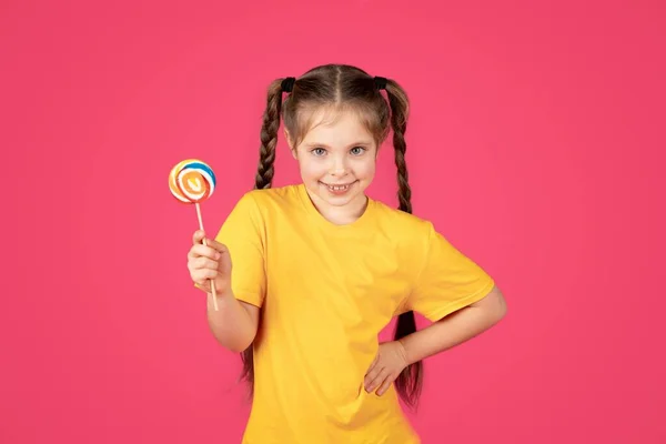 귀여운 귀여운 소녀가 웃으면서 롤리팝을 사탕을 아이를 카메라를 분홍색 스튜디오 — 스톡 사진