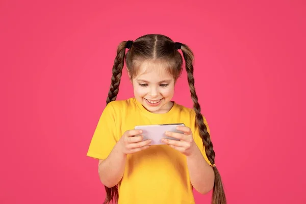 Веселая Девочка Подросток Играет Игры Смартфоне Стоя Розовом Фоне Студии — стоковое фото