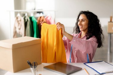 Kıyafet Tasarım Şirketi. Başarılı Tasarımcı Bayan Kapalı Masa 'da Oturan Alıcılar için Moda Giysi Paketleme Siparişi. Kendi Çevrimiçi Moda Dükkanı 'nda çalışan iş kadını. Ticaret Konsepti