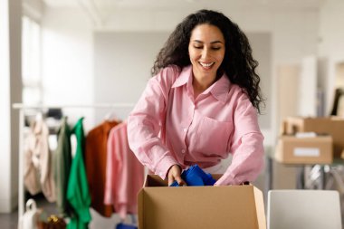 Başarılı perakende işi. Çevrimiçi Giyim Mağazası 'nda çalışan bir kadın, paket siparişi verilmiş kıyafet kutusunda kapalı teslim edilecek. Mutlu Dükkan Sahibi Müşteriler için Kıyafet Hazırlıyor