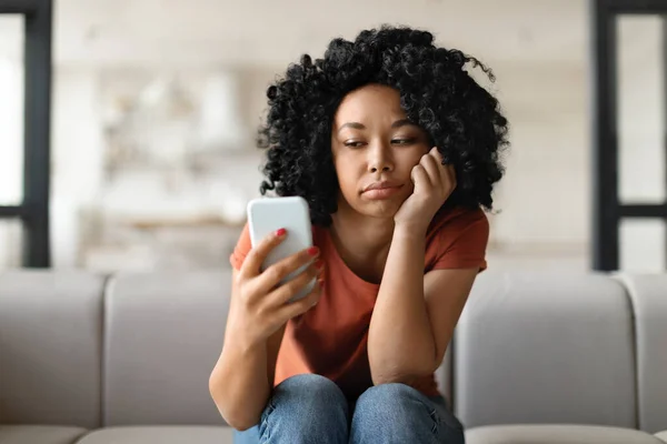 Evde Koltukta Otururken Akıllı Telefon Ekranına Bakan Genç Siyahi Kadın — Stok fotoğraf