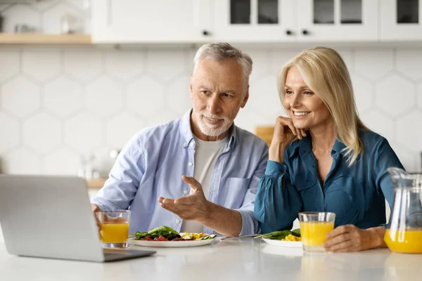 一緒に朝食をしながら キッチンでラップトップを使用して笑顔のシニアカップル 幸せな成熟した配偶者自宅でコンピュータで休んで 退職時間を楽しんで 無料のスペースで撮影されたクローズアップ — ストック写真