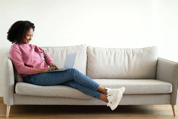 Позитивна Тисячолітня Афроамериканська Кучерява Дама Друкує Ноутбуці Спілкуючись Дивані Інтер — стокове фото