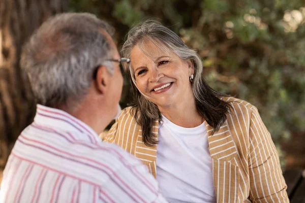 Smiling senior gray haired caucasian wife look at husband, talk in park outdoor, close up. Old couple enjoy walk, tender moment, date and active lifestyle, love and relationship