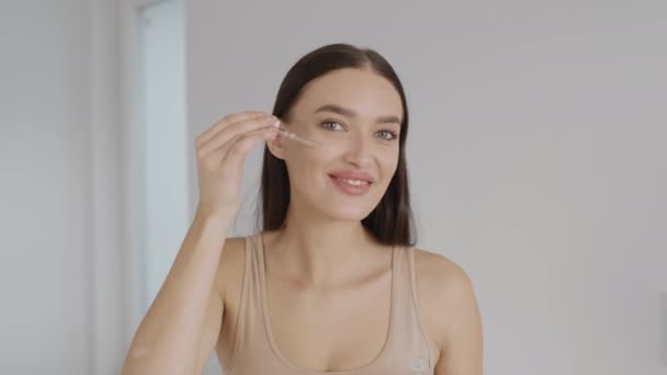 美容ブログ 顔の皮膚に栄養美容液を適用し それをこすり若い幸せな女性のカメラのポルノの肖像画 自宅でカメラに笑顔 — ストック動画