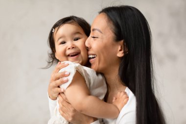 Kucaklaşma ve Neşe. Neşeli Japon anne, bebeğini kucaklıyordu, bebek yanaklarına burnunu sürtüyordu evde sevgi ve derin bir bağ kuruyordu. Şirin Annelik Anları