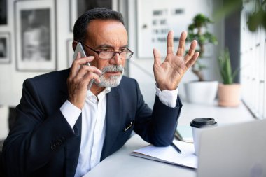 Üzücü, Avrupalı kıdemli takım elbiseli işadamı, ofis içi masasındaki akıllı telefondan dizüstü bilgisayarlı gözlüklü aramalar. Hata, iş sorunları, uzaktan iş, teknoloji ile başlangıç