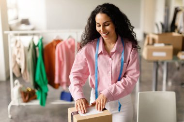 Kendi Giyim Markası. Neşeli Moda Tasarımcısı Kadın Kapalı Kapılar 'da çalışıyor, sipariş edilmiş kıyafetlerle paket yapıyor. Moda Şov Salonu Sahipliği, İş ve Ticaret