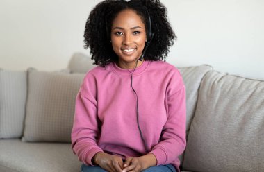 Gülümseyen milenyum Afro-Amerikan kıvırcık kadın menajeri oturma odasının iç kısımlarında danışmanlık yapan bir müşteri. Video çağrısı, uzaktan iletişim, evde çalışma, müşteri desteği