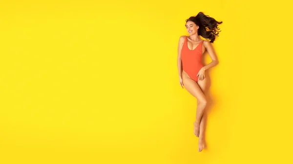 夏の美人募集 黄色のスタジオを背景にテキスト 日光浴 休暇でリラックスのための無料スペースの近くに横たわるオレンジワンピース水着で女性 パノラマ ビューショットの上 — ストック写真