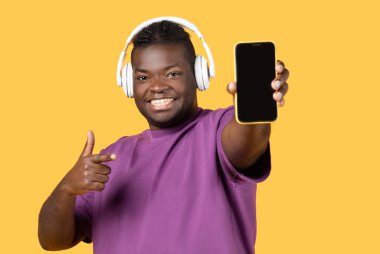 Müzik aletleri. Sarı Stüdyo Arkaplanında Müzik Uygulamasını Onaylayan, Akıllı Telefon Boş Ekran Gösteren Neşeli Siyah Adam. Cep telefonunda Şarkı Dinleyen Adam