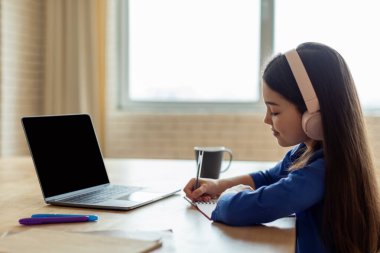 E-Öğrenme Teklifi. Yan görüntüde, liseli kız dizüstü bilgisayarında boş kulaklıkla not alırken, internette öğrenirken ve evde ödev yaparken görülüyor. Model