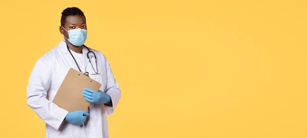 医务人员 自信的非洲裔美国医生 身穿面罩 白色外套和橡胶手套 手持剪贴板站在黄色工作室背景 复制空间 — 图库照片