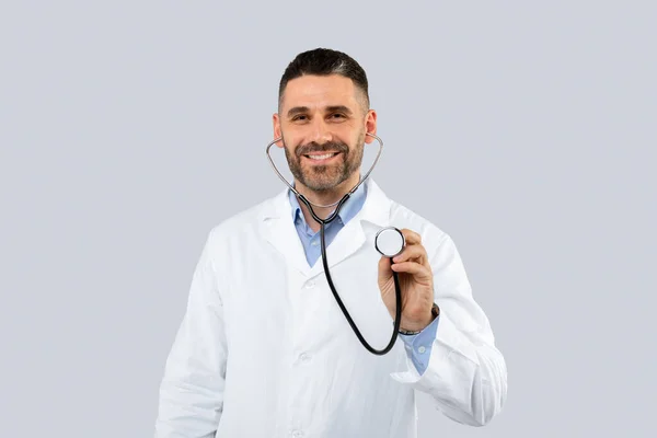 光スタジオの背景に白い医療コートを着た優しい中年男性医師は 聴診器と笑顔を使用して スペースをコピーします 仕事と職業 — ストック写真