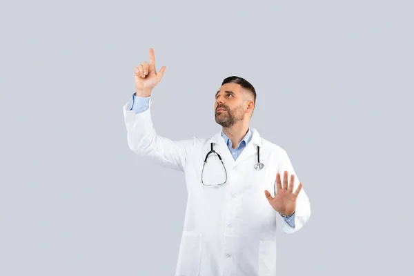 自信的中年男性治疗师 身穿白色外套 手握空空的屏幕 背景浅灰 医药和治疗的现代技术 — 图库照片