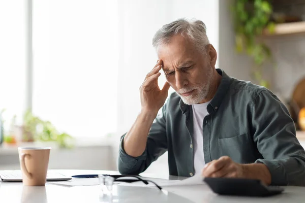 Stressad Senior Man Kontrollera Papper Medan Sitter Vid Skrivbordet Köket — Stockfoto