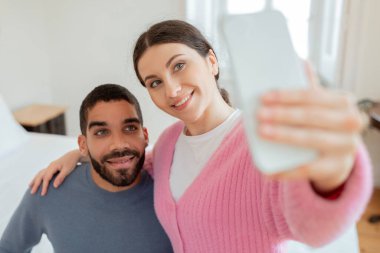 Sosyal medya varlığı. Neşeli blogcular, Selfie Çeken Akıllı Telefon Yapan, Modern Yatak Odası İçi 'nde Poz Veren Çift. Genç Eşlere Seçici Odaklanma. Gadgets ve Çevrimiçi Eğlence