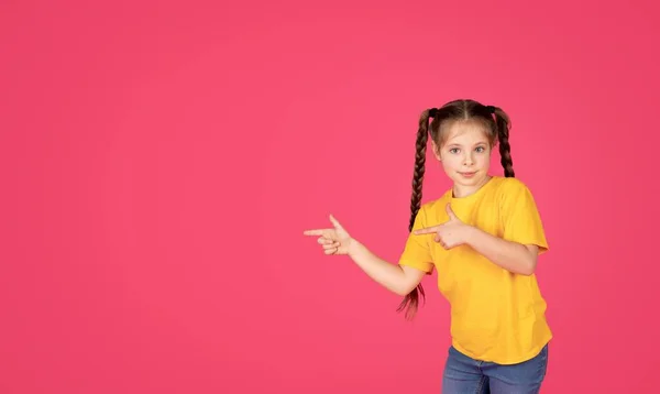 いい提案だ 2本の指で脇を指差す可愛い女の子 ピンクのスタジオの背景に広告デザインのためのコピースペースを示すかわいい十代の女性の子供を笑顔 パノラマ — ストック写真