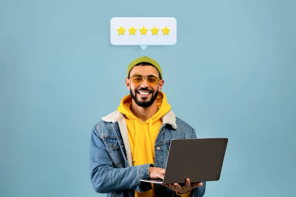 stock image Great Website Rating. Customer Guy With Laptop And Five Star Feedback Above Head Posing On Blue Studio Background. Man Browsing Internet Sending Excellent Review Advertising Best Website. Collage