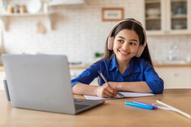 E-Öğrenme Teklifi. Diz üstü bilgisayarda ödevlerini yapan, kablosuz kulaklık takan ve evde not alan neşeli okul çocuğu. Liseli Kız Bilgisayardan Sanal Ders İzliyor. Çalışma ve Aletler