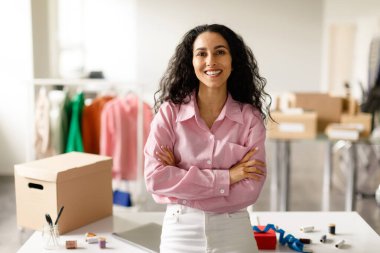 Moda sektörü başarısı. Başarılı Giysi Tasarımcısı Kadın, Showroom 'daki kıyafetlerle dolu rafın yanında gülümseyen kameraya gülümsüyor. Mutlu Giysi Mağazası Sahibi Kadın. Perakende ve Ticaret