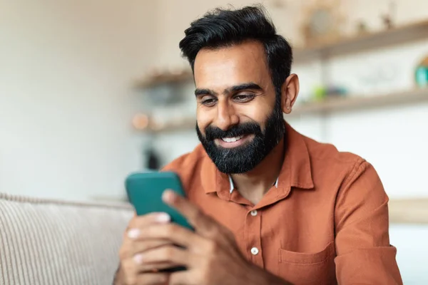 stock image Portrait Of Happy Indian Man Using Smartphone With New Application, Communicating And Having Fun Playing Game Online Sitting On Sofa At Home. Internet, Communication Offer Concept