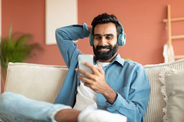 Avslappnad Indisk Skäggig Man Med Smartphone Och Hörlurar Lyssna Musik — Stockfoto