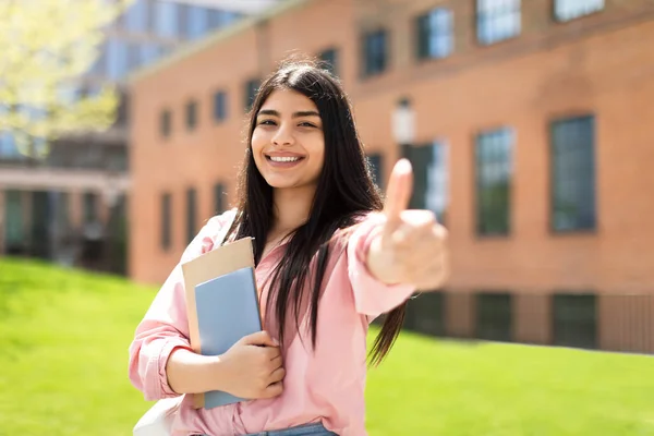 笑顔のヒスパニック系の学生の女の子は 親指のジェスチャーを表示し カメラで笑顔 大学のキャンパスに立って 正の女性は ワークブックを保持します 教育プログラムをお勧めします — ストック写真