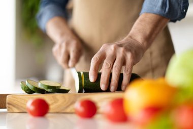 Sağlıklı beslenme. Mutfakta tanınmayan bir adam sebze pişirirken, erkek aşçının önlük keserken, kabak keserken, öğle yemeği pişirirken ya da evde akşam yemeği yerken, bıçakla, kırbaçlanırken yakın plan fotoğrafı.