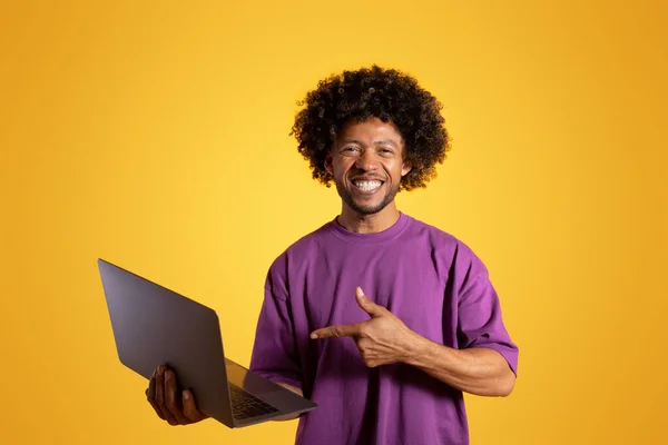 보라색 티셔츠를 곱슬곱슬 남자가 주황색 스튜디오에 고립된 노트북에 손가락을 있습니다 — 스톡 사진