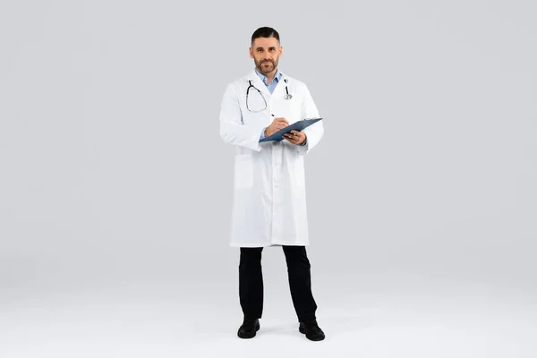 Läkarkonsultation Medelålders Man Läkare Uniform Innehav Urklipp Och Tittar Kameran — Stockfoto