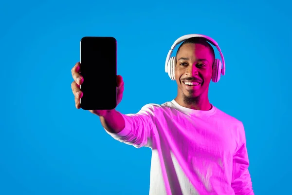 Koncepcja Aplikacji Muzycznych Wesoły Przystojny Młody Czarny Mężczyzna Pokazuje Smartfon — Zdjęcie stockowe