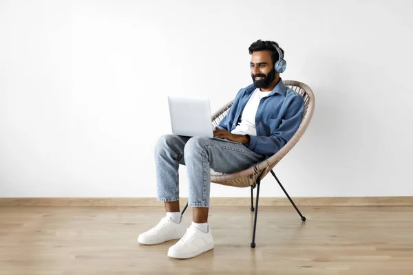 Leende Arabisk Man Arbetar Laptop Bär Hörlurar Sitter Fåtölj Nära — Stockfoto