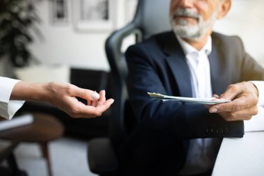 Gülümseyen Avrupalı kıdemli iş adamı masada oturuyor, kadınlara ofis içi el ele para veriyor, kırpılıyor, kapanıyor. İş için maaş, mali kazanç, iş başarısı