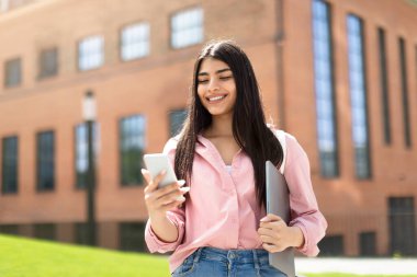 Çalışmak için sosyal ağlar. Elinde telefon ve dizüstü bilgisayarı olan mutlu bir bayan öğrenci üniversitede ders vermeye hazır, dışarıda bekliyor. Aygıt, bilgi, modern eğitim, seminer ve sınav hazırlığı