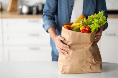 Sağlıklı Beslenme Konsepti. Mutfak içlerine poşet dolusu yiyecek koyan olgun bir adam, taze organik sebzeler ve meyvelerle tanınmayan son sınıf erkek paketleri koyuyor.
