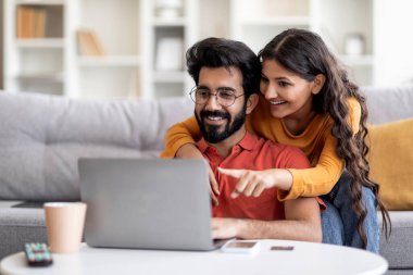 Genç Hintli eşler evde dizüstü bilgisayarla rahatlarken mobilya seçiyor, mutlu doğu çifti birlikte internet alışverişi yapıyor, alışveriş yapıyor, bilgisayar ekranını işaret eden kadınlar...