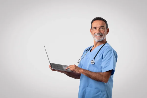 Χαρούμενος Καυκάσιος Ώριμος Άντρας Γιατρός Μπλε Στολή Δακτυλογραφεί Στον Υπολογιστή — Φωτογραφία Αρχείου