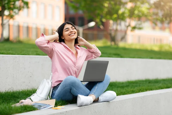 休息一下快乐的少女轻松地坐在公园里使用笔记本电脑 快乐的女性舒展筋骨 享受远程教育 感到快乐和满意 自由自在 — 图库照片