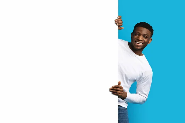これを調べてくれ 陽気なハンサムな若いですアフリカ系アメリカ人男でカジュアル立ってによってホワイトブランク広告ボードと笑顔でカメラ 隔離されたオンブルースタジオの背景 — ストック写真