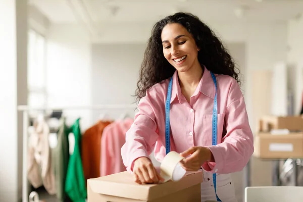 Fashion Commerce. Happy Woman Designer Packing Cardboard Boxes With Clothes For Fashion Store Clients Working In Clothing Boutique Indoor. Successful Small Retail Business Concept