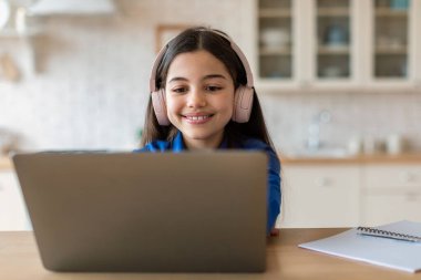 E-öğrenmenin neşesi. Bilgisayarda kulaklık takan, evde oturup bilgisayar okuyan mutlu liseli kız internette geziniyor. Eğitim ve Gadget 'lar. Mesafe Öğrenme Konseptinin tadını çıkar
