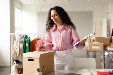 Moda Tasarım Şirketi. Başarılı Ortadoğulu Kadın Çevrimiçi Giyim Mağazasında çalışıyor, Giysileri Kutulara Paketliyor, Panoya Yazıyor, Müşterilerin Moda Şovu Siparişlerini Kontrol Ediyor