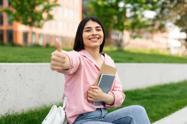 興奮した学生の女性親指をジェスチャーし 本を保持ポーズ 大学のキャンパスや公園に座って 私は大学が好きです近代教育の概念を承認する女の子は — ストック写真